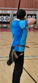 Une archère en train de viser, vue de dos, lors d'un concours en salle.